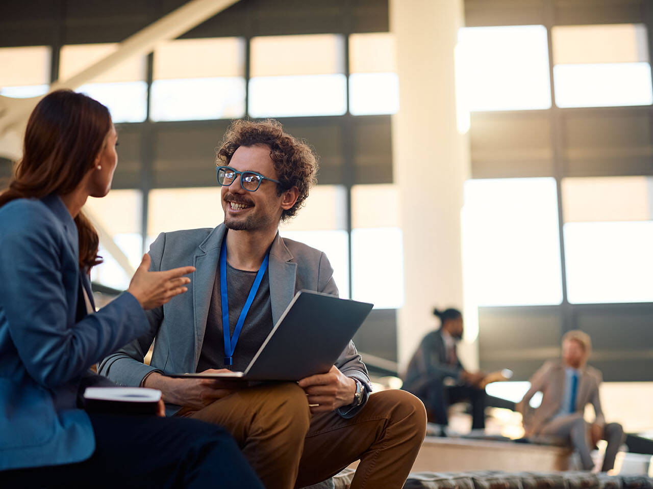 Happy businessman talking to female colleague while using laptop in convention center.